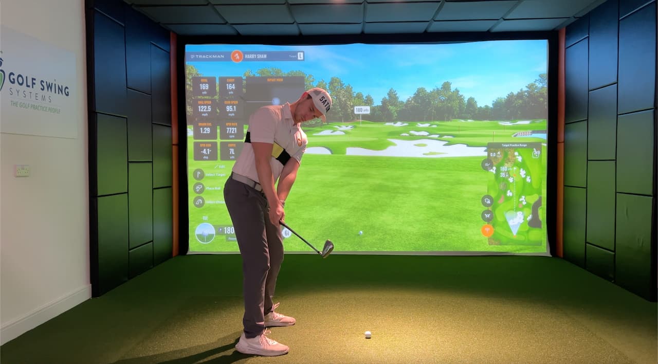 Person playing a golf simulation game in a room with a large screen displaying a golf course.